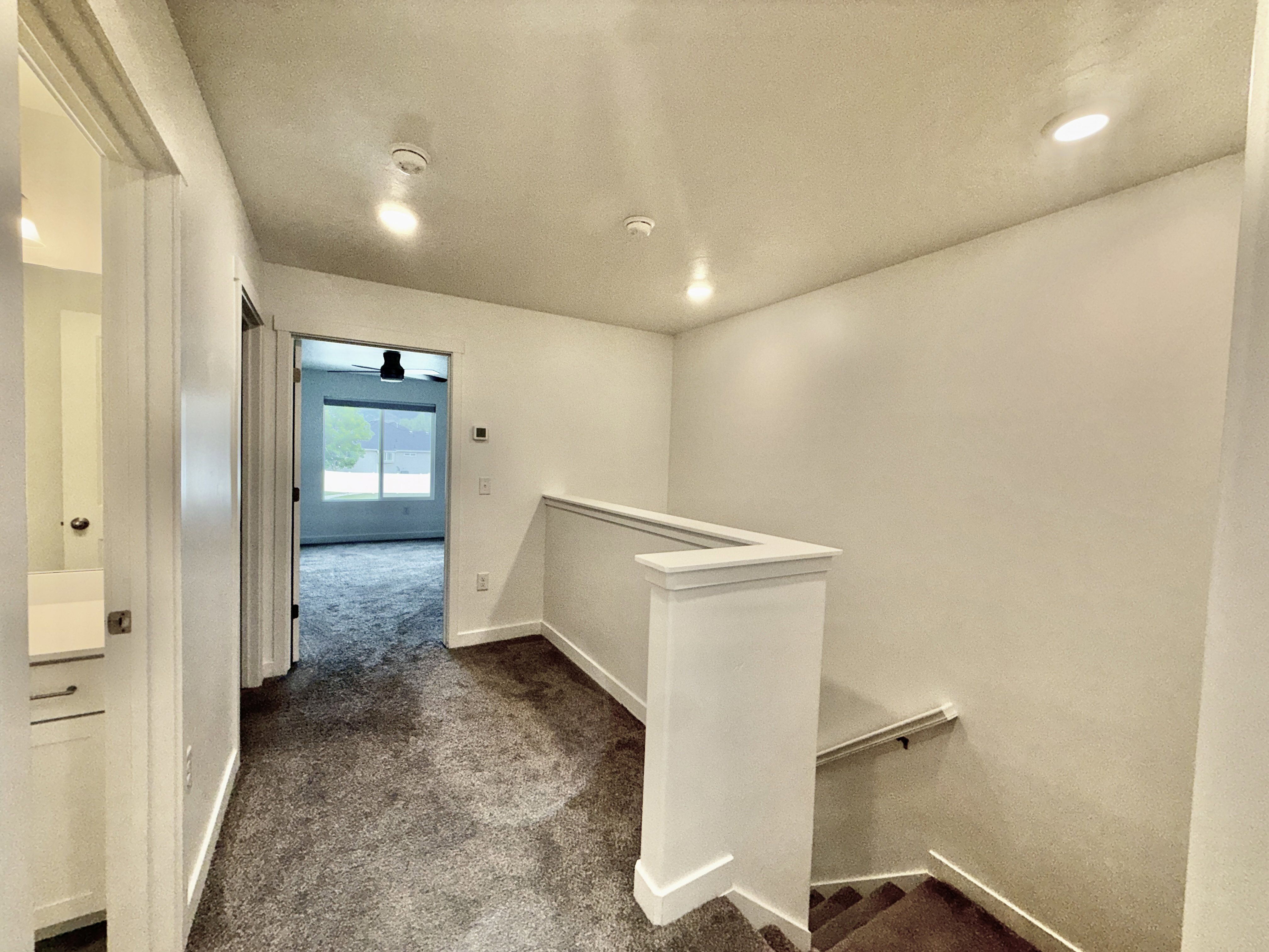 Upper-level hallway featuring textured carpet flooring, recessed lighting, and a white painted banister with a metal handrail