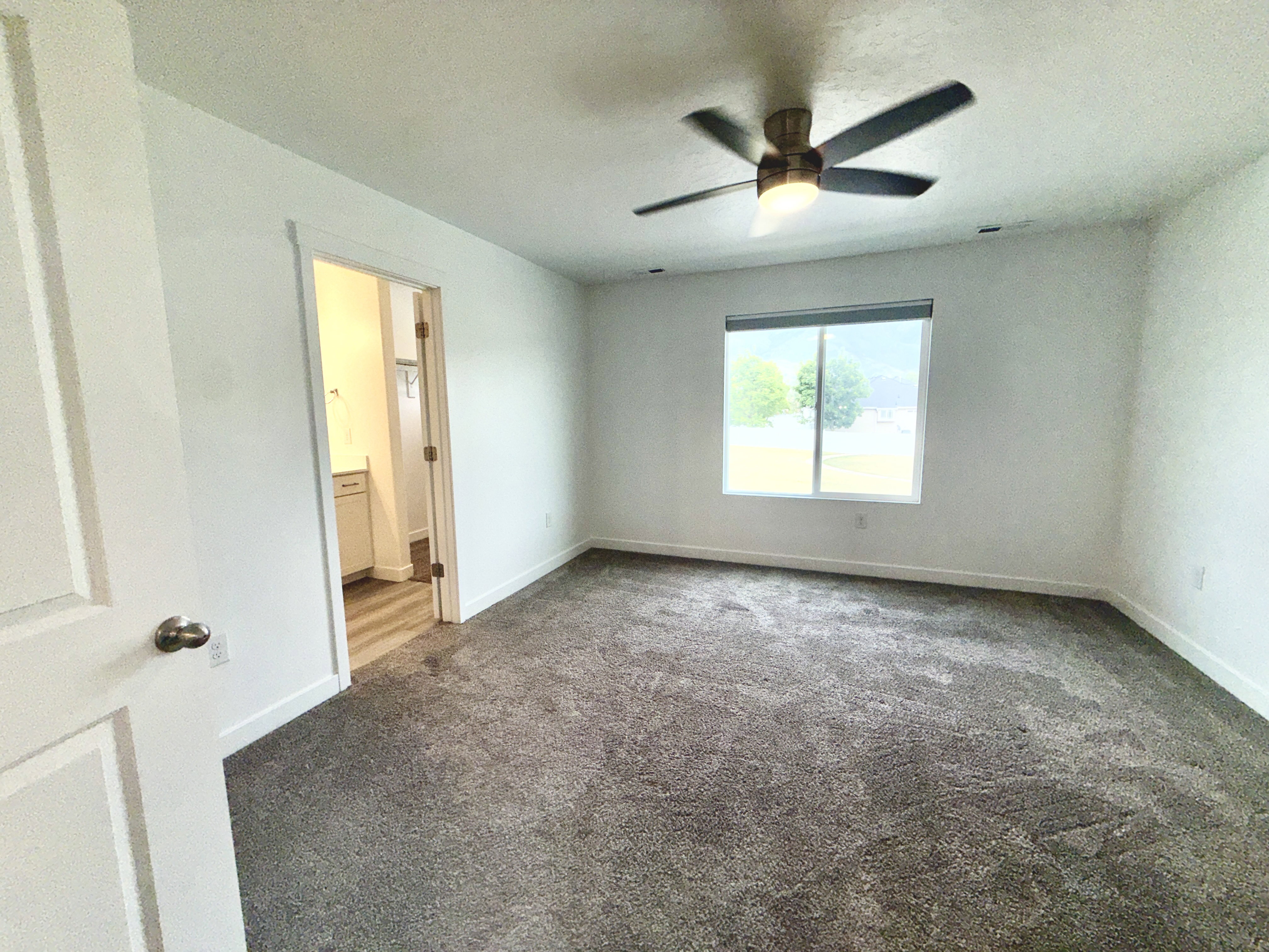 Spacious room featuring neutral carpeting, a ceiling fan with integrated lighting, and a large window