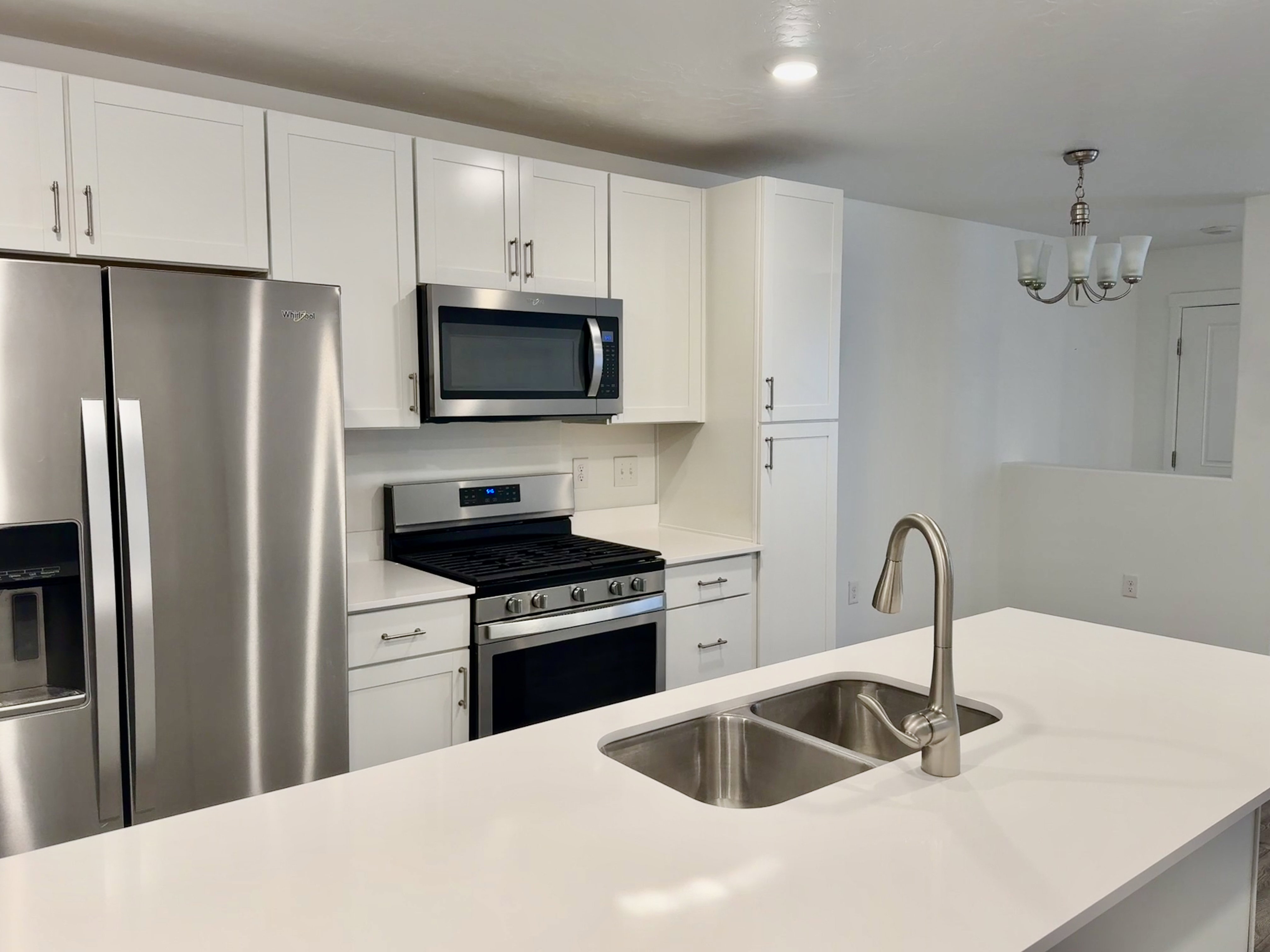Modern kitchen featuring white shaker cabinetry, stainless steel appliances including a side-by-side refrigerator, over-the-range microwave, and gas range