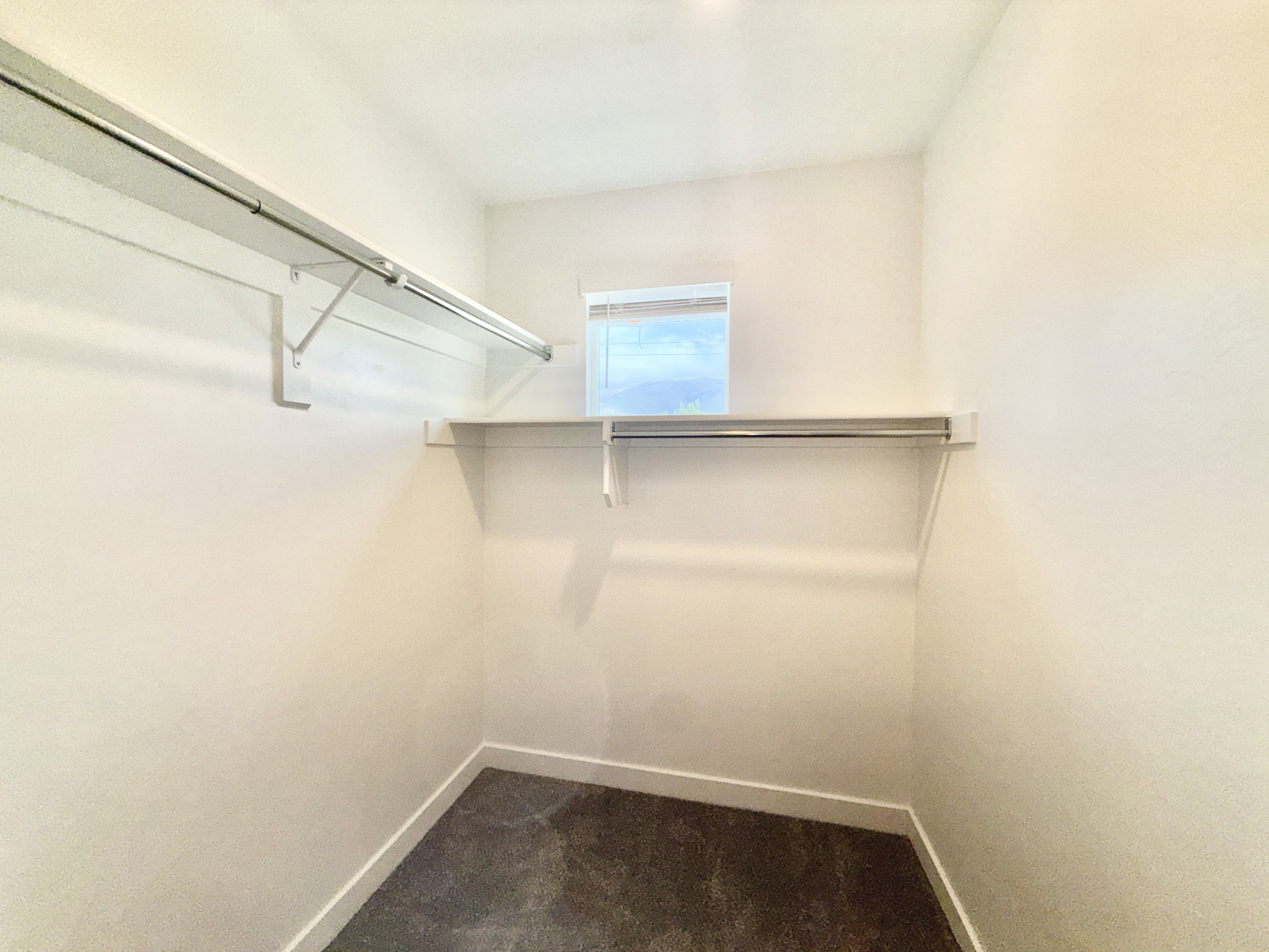 Walk-in closet featuring dual hanging rods, upper shelving, a window, dark flooring, and white baseboards