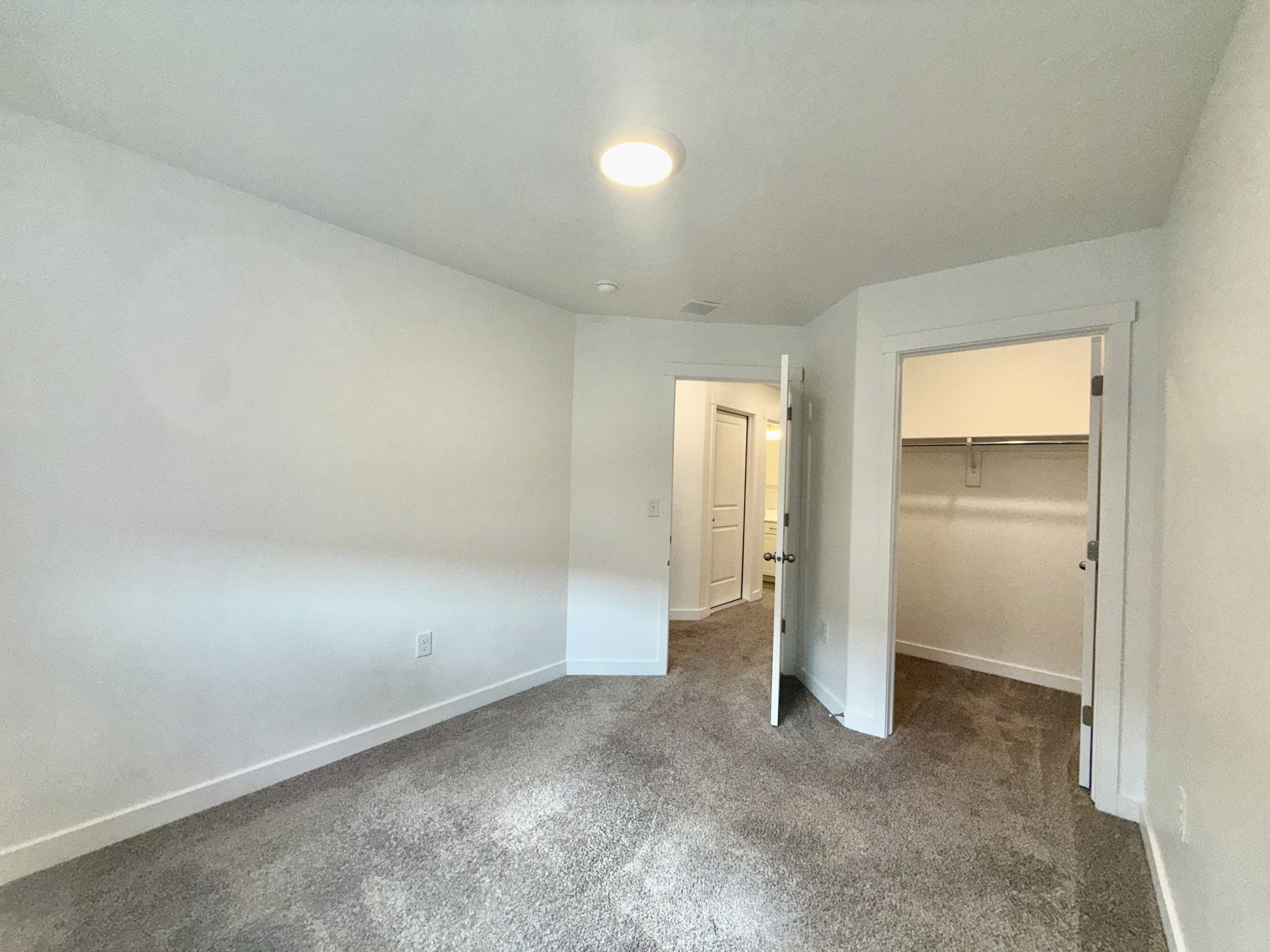 Carpeted room with white walls, a single ceiling light fixture, a closet with shelving and a hanging rod, and a white interior door
