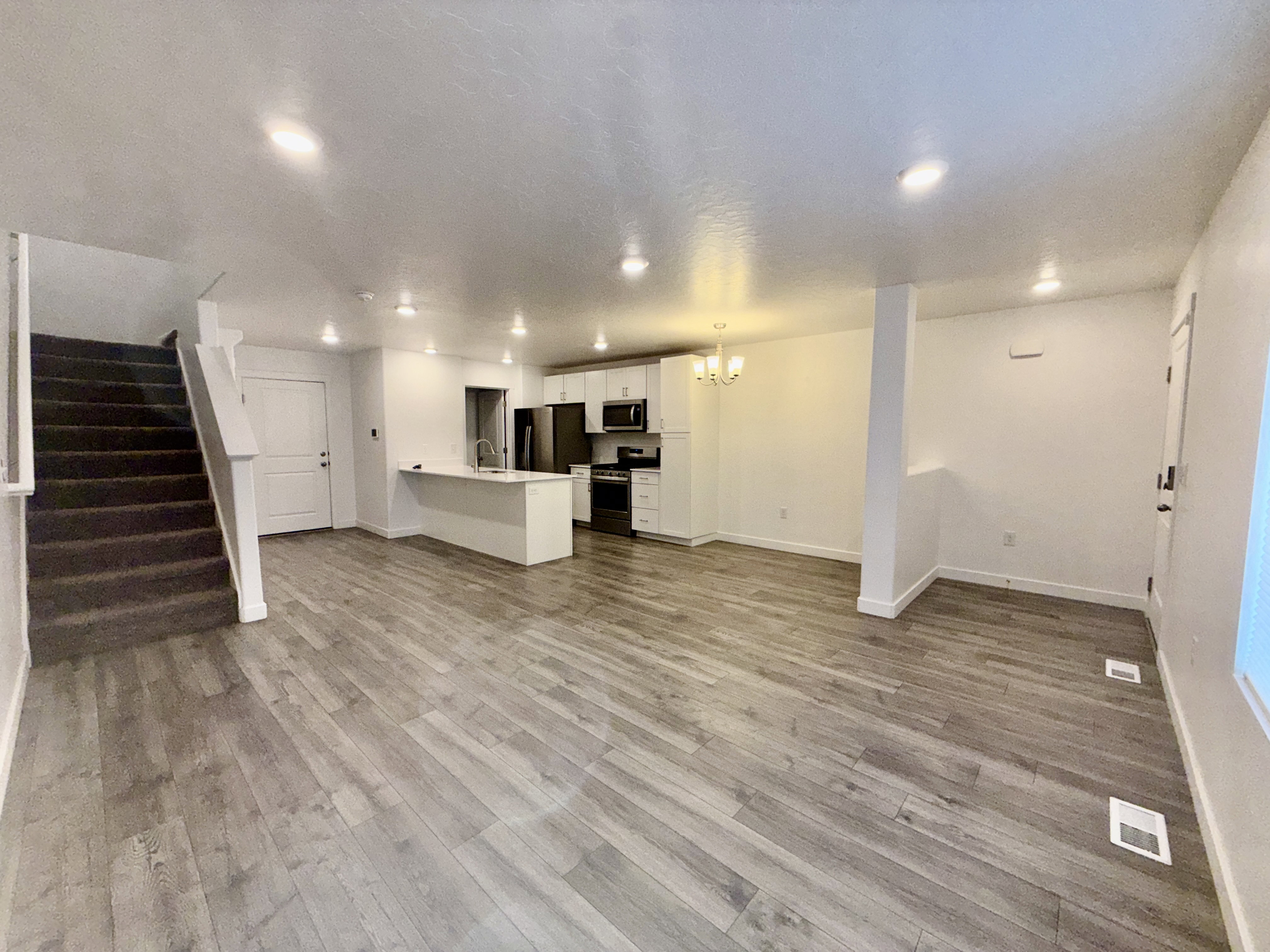 Open-concept living space featuring wood-finish flooring, recessed lighting, and a modern kitchen with white cabinetry and dark appliances