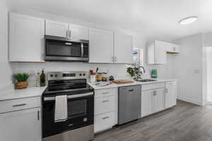 Kitchen with appliances with stainless steel finishes, light countertops, white cabinetry, and wood finished floors