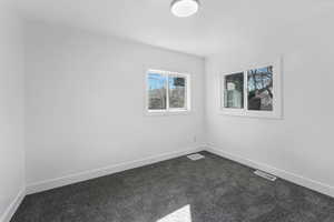 Empty room featuring baseboards, visible vents, and dark colored carpet