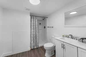 Full bathroom featuring toilet, curtained shower, wood finished floors, and visible vents