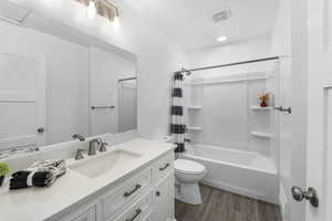 Bathroom featuring visible vents, toilet, shower / tub combo, vanity, and wood finished floors