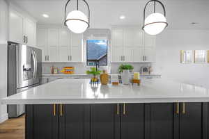 Kitchen featuring white cabinets, light countertops, a large island, stainless steel refrigerator with ice dispenser, and tasteful backsplash