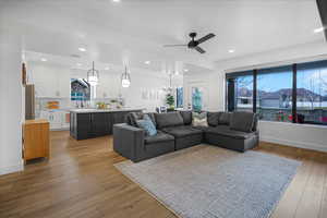 Living room with recessed lighting, light wood-style flooring, baseboards, and ceiling fan with notable chandelier