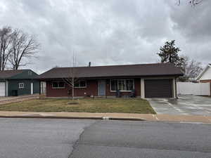 Ranch-style home with an attached garage, fence, concrete driveway, a gate, and a front lawn