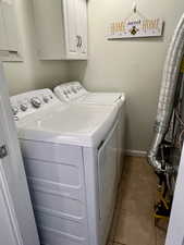 Laundry area featuring tile patterned flooring, washing machine and dryer, cabinet space, and baseboards