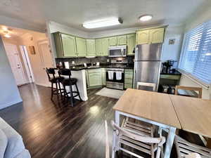 Kitchen with dark wood finished floors, green cabinetry, appliances with stainless steel finishes, ornamental molding, and backsplash