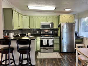 Kitchen with stainless steel appliances, dark countertops, green cabinetry, and a peninsula