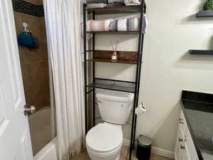 Bathroom featuring shower / tub combo, toilet, and baseboards