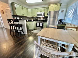 Kitchen featuring dark wood-style flooring, green cabinets, appliances with stainless steel finishes, tasteful backsplash, and dark countertops