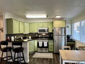 Kitchen with dark countertops, appliances with stainless steel finishes, dark wood-type flooring, a peninsula, and green cabinets