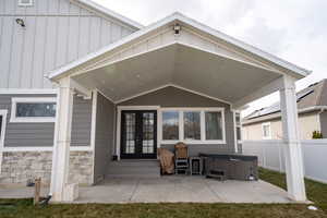 Back of property featuring a hot tub, a patio, fence, french doors, and board and batten siding