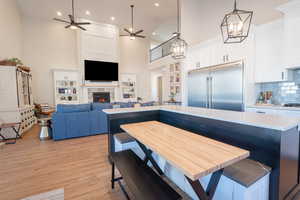 Dining room with a tile fireplace, light wood-style flooring, recessed lighting, ceiling fan with notable chandelier, and a high ceiling