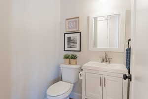 Half bathroom with toilet, baseboards, and vanity