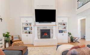 Living area with beautiful custom cabinetry, a fireplace, light wood-style flooring, and a towering ceiling