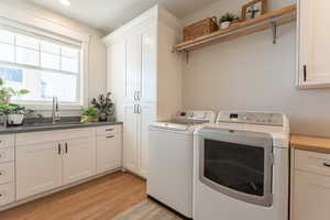 Clothes washing area with cabinet space, light wood finished floors, independent washer and dryer, A SINK and NATURAL LIGHT, and beautiful custom cabinetry.