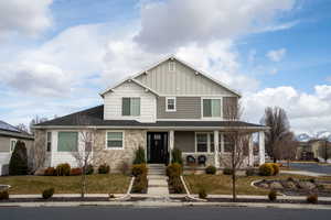 View of front facade featuring covered porch, stone siding, a front lawn, and board and batten siding