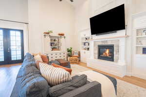 Living room featuring beautiful custom built in features, french doors, light wood-style floors, a stone fireplace, and high vaulted ceiling