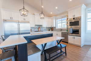 Kitchen featuring lofted ceiling, stainless steel professional  appliances (yes, the refrigerator is really that big), a sink, beautiful custom white cabinetry, and tasteful backsplash.