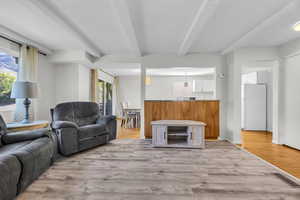 Living area with light wood-style floors, visible vents, and beam ceiling