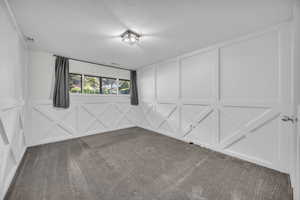 Carpeted empty room with a textured ceiling, a decorative wall, and visible vents