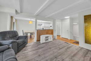 Living area with light wood-style floors, visible vents, and beam ceiling