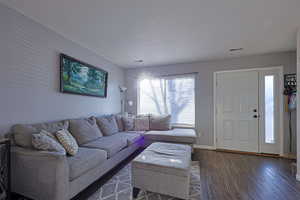 Living room featuring dark wood-style floors, a textured ceiling, visible vents, and baseboards