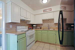 Kitchen with tasteful backsplash, white electric range, light tile patterned flooring, a sink, and under cabinet range hood