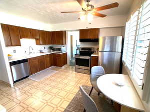 Kitchen featuring light floors, light countertops, under cabinet range hood, a ceiling fan, and stainless steel appliances