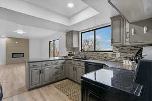 Kitchen with gray cabinetry, a peninsula, a fireplace, a sink, and black appliances