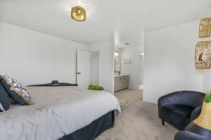 Bedroom featuring baseboards, ensuite bathroom, and light colored carpet