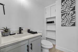 Bathroom with toilet, baseboards, wood finished floors, and vanity