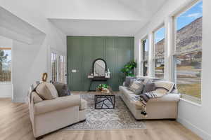 Living area featuring vaulted ceiling, a decorative wall, baseboards, and wood finished floors