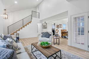 Living room featuring light wood-style flooring, an inviting chandelier, high vaulted ceiling, baseboards, and stairs