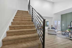 Staircase featuring french doors, a high ceiling, wood finished floors, and baseboards