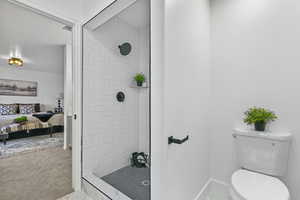 Bathroom featuring baseboards, tiled shower, toilet, and ensuite bathroom