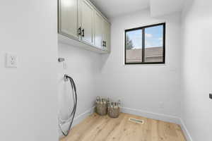 Clothes washing area with wood finished floors, cabinet space, and baseboards