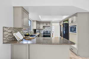 Kitchen featuring a peninsula, a sink, appliances with stainless steel finishes, backsplash, and a raised ceiling