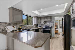 Kitchen featuring a raised ceiling, backsplash, a sink, a peninsula, and black appliances