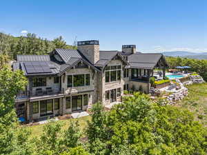Back of property with a standing seam roof, a chimney, roof mounted solar panels, a metal roof, and stone siding