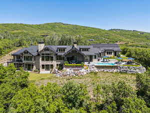 Rear view of house featuring a chimney, a standing seam roof, stone siding, and an outdoor pool