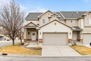 View of front of house with driveway, stone siding, and roof with shingles