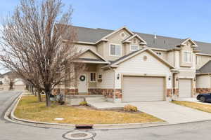 View of front of house with a shingled roof, stone siding, driveway, and a front lawn