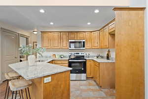 Kitchen featuring appliances with stainless steel finishes, a peninsula, a kitchen bar, a sink, and recessed lighting