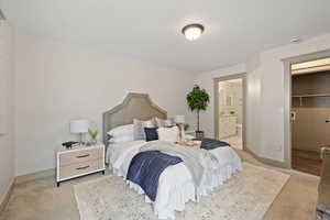 Carpeted bedroom with ensuite bathroom, a walk in closet, and baseboards
