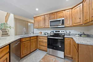 Kitchen with stainless steel appliances, light stone counters, a sink, and brown cabinets